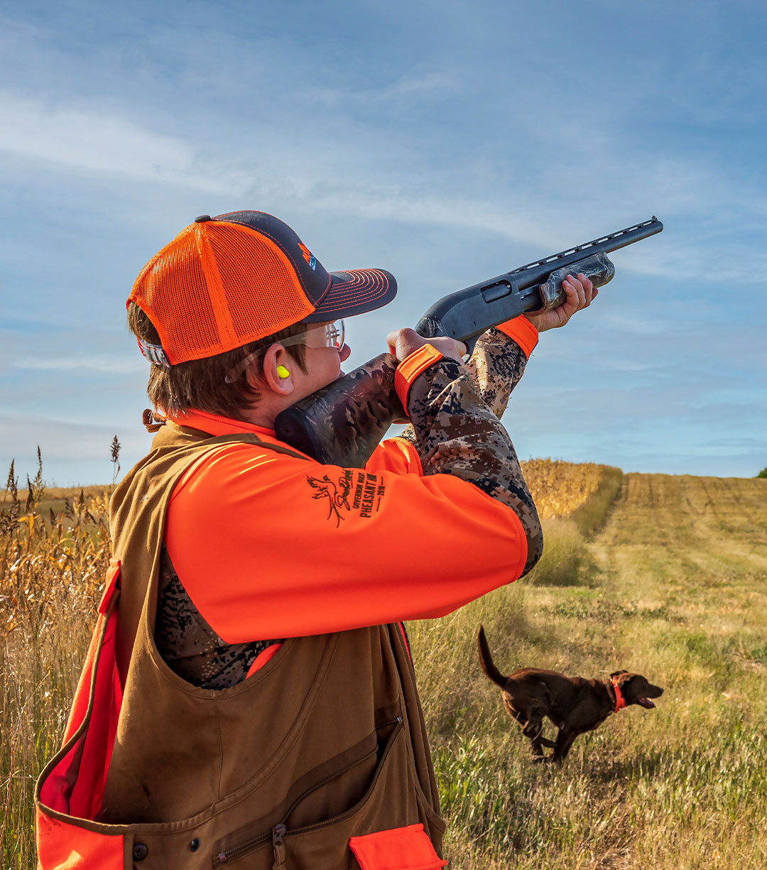 young boy in hunter orange pointing a gun to the sky