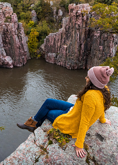 a girl sitting on the edge of a rock looking at the water